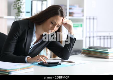 Donna di bookkeeper preoccupata che calcola sulla calcolatrice seduta su una scrivania in ufficio Foto Stock