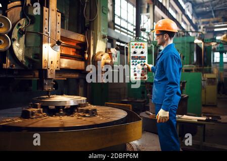 Turner in uniforme e casco funziona su tornio grande, fabbrica. Produzione industriale, ingegneria metallurgica, produzione di macchine elettriche Foto Stock