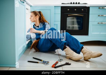 Carino idraulico femminile in uniforme tiene tubo di scarico in cucina. Handycam con lavello per la riparazione delle borse, servizio di assistenza sanitaria a casa Foto Stock