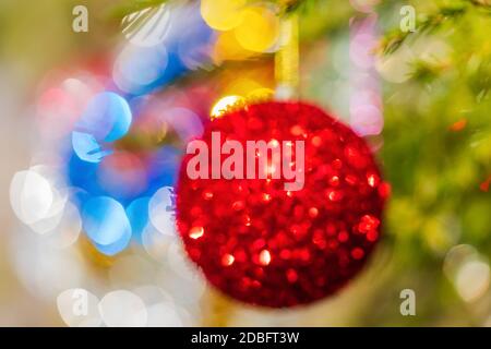 Pallina di Natale rossa sfocata appesa al ramo del pino di Natale. Bokeh offuscato creativo colorato astratto. Composizione vacanza fuori fuoco Foto Stock