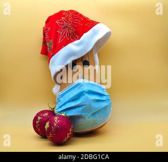 zucca in maschera a causa del covid con cappello e. decorazioni natalizie isolate su sfondo arancione neutro Foto Stock