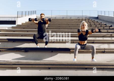 Coppia sportiva in abbigliamento sportivo che fa squat con manubri all'aperto scale della città Foto Stock