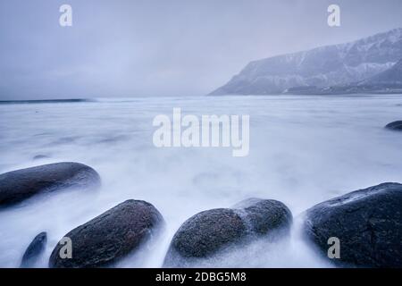 Onde di mare norvegese che si staglia su rocce di pietra a Unstad spiaggia, Lofoten isole, Norvegia in tempesta invernale. Esposizione lunga Foto Stock