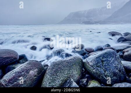 Onde di mare norvegese che si staglia su rocce di pietra a Unstad spiaggia, Lofoten isole, Norvegia in tempesta invernale. Esposizione lunga Foto Stock