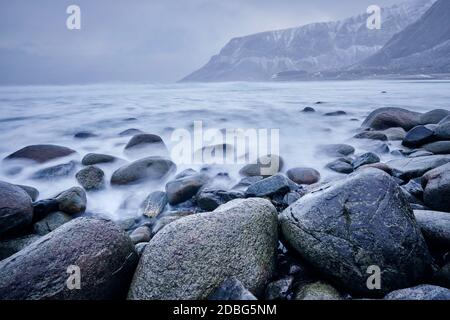 Onde di mare norvegese che si staglia su rocce di pietra a Unstad spiaggia, Lofoten isole, Norvegia in tempesta invernale. Esposizione lunga Foto Stock