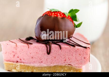 Torta al soufflé di yogurt decorata con fragole in cioccolato su a. piatto con un bicchiere di latte Foto Stock