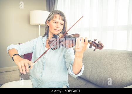 Donna matura che gioca violino nel suo appartamento urbano Foto Stock