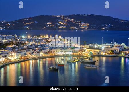 Vista della città di Mykonos Chora destinazione turistica turistica turistica turistica di vacanza con famosi mulini a vento, e porto con barche e yacht illuminati in serata Foto Stock