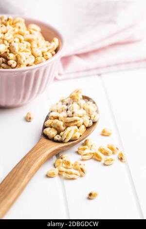 Grano soffiato coperto di miele in cucchiaio di legno su tavola bianca. Foto Stock