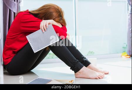 Asian giovane donna triste abbracciare il suo ginocchio e gridare indossando maschera facciale protettiva disoccupato quarantine malattia coronavirus o COVID-19 sua seduta da sola su fl Foto Stock