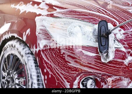 Dettaglio sulla luce rossa dell'auto lavata in autolavaggio, colpi di sapone bianco sulla superficie. Foto Stock