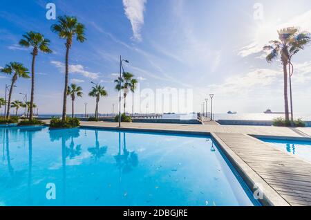 Molos Promenade e sullo skyline della costa nella città di Limassol a Cipro a sunrise. Vista sul Boardwalk pier pietra miliare del percorso con palme, piscine di wat Foto Stock
