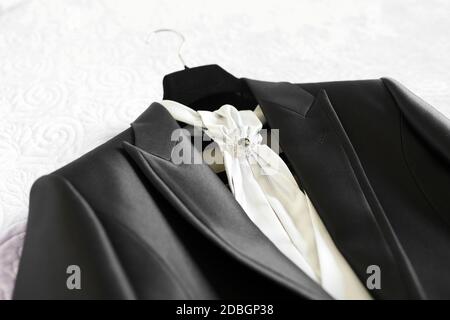 Abito da sposa e accessori per lo sposo con cravat bianco e puntate su un appendiabiti pronto per la cerimonia di matrimonio Foto Stock