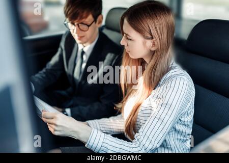 Immagine di un giovane uomo d'affari, di un uomo e di una donna in abiti ufficiali, seduti in un'auto con documenti di lavoro Foto Stock