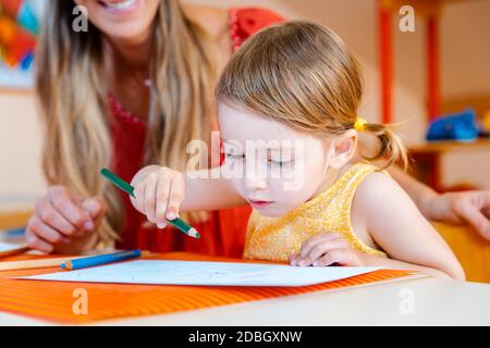 I bambini che disegnano con matite nella scuola di gioco, l'insegnante aiuta Foto Stock