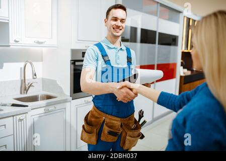 Idraulico maschile in uniforme e cliente femminile in cucina. Handyman con lavello di riparazione della borsa degli attrezzi, servizio di attrezzatura sanitaria a casa Foto Stock