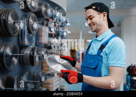 Lavoratore maschile in uniforme scelta del disco refilato per sega in magazzino utensili. Scelta di attrezzature professionali nel negozio di ferramenta, supermercato di strumenti Foto Stock