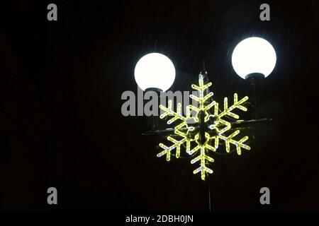 Le figure di Natale sopra i plafonds luminosi sul palo nella notte. Luci natalizie e di Capodanno. Garland a forma di fiocco di neve nel parco cittadino. Foto Stock