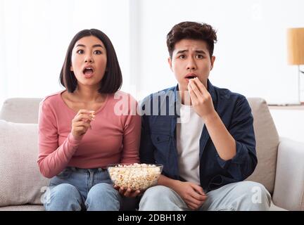 Una coppia coreana scioccata guardando un film televisivo seduto nel soggiorno Foto Stock