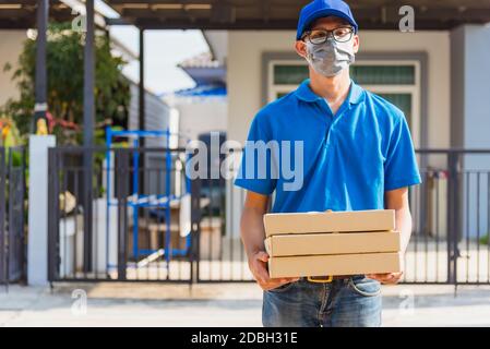 Asian giovane consegna uomo Courier on-line con l'ordine di cibo è pizza scatole in uniforme lui maschera protettiva viso, cliente di servizio di fronte alla casa unde Foto Stock