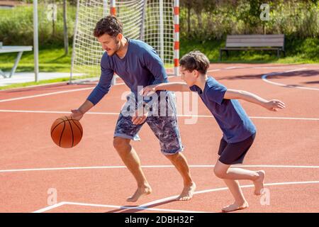 Padre e figlio giocano a basket a piedi nudi in un parco giochi Foto Stock