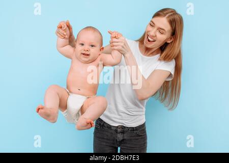 Felice famiglia. Una madre ridente solleva delicatamente il suo adorabile figlio neonato nell'aria, contro uno sfondo blu isolato Foto Stock