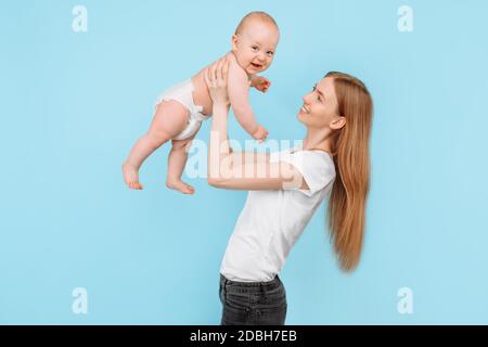 Felice famiglia. Una madre ridente solleva delicatamente il suo adorabile figlio neonato nell'aria, contro uno sfondo blu isolato Foto Stock