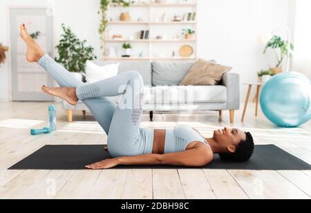 Allenamento sportivo a casa. Bella giovane donna sdraiata sul tappeto yoga e ciding in aria, facendo esercizio abs in soggiorno Foto Stock