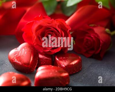 Il giorno di San Valentino rose con nastro rosso e hart cioccolato modellato su sfondo grigio Foto Stock