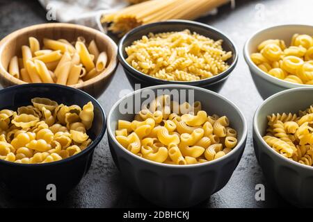 Vari tipi di pasta italiana cruda in ciotole su tavola da cucina. Foto Stock