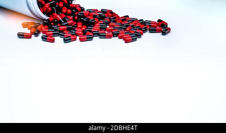 Pillole di capsula di antibiotico rosso-nero sparso fuori del flacone di droga di plastica su sfondo bianco. Resistenza agli antibiotici. Industria farmaceutica. Farmacia Foto Stock