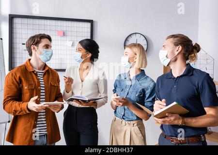 giovani uomini d'affari multiculturali in maschere mediche che discutono di progetto d'impresa Foto Stock