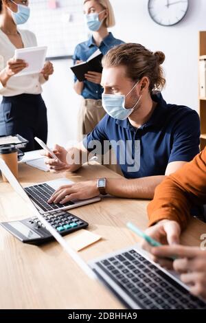 giovane squadra di uomini d'affari multiculturali in maschere mediche che lavorano insieme in ufficio open space Foto Stock