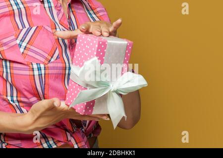 Confezione regalo con pois rosa con nastro di seta bianco retro modello donna mani su sfondo giallo Foto Stock