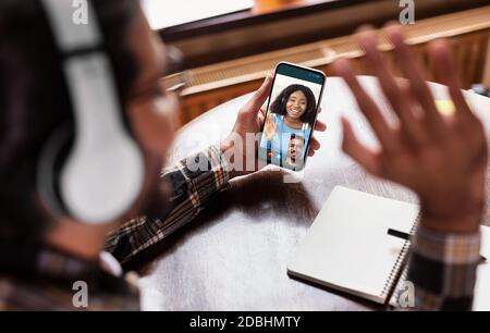 Uomo irriconoscibile che saluta il cellulare facendo videochiamata in interni Foto Stock