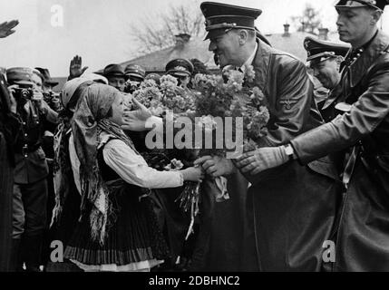 Adolf Hitler patte la guancia di una bambina che lo presenta con un mazzo di fiori. Alle spalle di Hitler Julius Schaub. Maribor - Marburg an der Drau tedesco-austriaco - è stata una città di lingua tedesca in Austria-Ungheria fino al 1918. Foto Stock