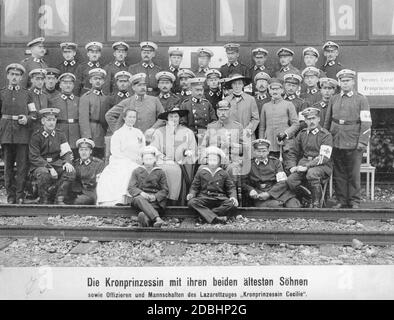 'Corona la principessa Cecilie di Mecklenburg (al centro della foto, seduta e indossata un cappello da donna) con i suoi due figli più anziani Wilhelm (a sinistra) e Luigi Ferdinando di Prussia (a destra), che sono seduti davanti a lei sulle tracce. Si pongono insieme a ufficiali e squadre di paramedici di fronte all'ambulanza n. 25 del treno ospedaliero di associazione ''Kronprinzessin Cecilie''. Questo treno è stato operato da Walter von Oettingen per la Croce Rossa. È sulla sinistra dietro Cecilie. Di fronte a lui è probabilmente sua moglie, Elisabeth von Oettingen. La foto è stata scattata nel 1916." Foto Stock