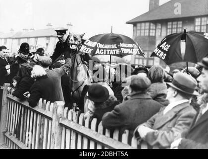 Ufficiali di polizia montati cercano di disperdere una dimostrazione in Denmark Street, nell'East End di Londra. La gente sta manifestando contro Lady Astor, deputato di Sutton, che è apparso a East End per l'apertura di nuove case dell'Esercito della Chiesa. Altri manifestanti (con ombrelli) dimostrano anche un aumento delle pensioni. Foto Stock