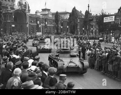 'Prima del 'giorno del Wehrmacht' al Congresso del Partito nazista di Norimberga una colonna di nuovi carri armati (Panzerkampfwagen i) scorre attraverso il centro della città, qui alla Bahnhofsplatz (sullo sfondo è l'edificio della stazione decorato con bandiere di swastika). Un cartello sulla destra indica la fermata Koenigstor, punto d'imbarco per Zeppelinwiese a Marientor'' in due minuti a piedi. I carri armati portano ancora la ''vernice colorata'' come camuffamento, che era comune fino alla metà degli anni 30, riconoscibile dai motivi di fleck.' Foto Stock