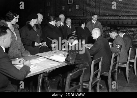 Gli elettori guardano alle liste elettorali per le elezioni del Reichstag e al referendum sul ritiro dalla Lega delle Nazioni del 12.11.1933 per verificare se sono in lista. Tra i lavoratori elettorali c'è un nazionalsocialista. Foto Stock