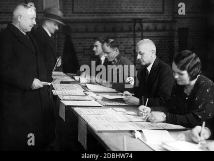 Gli elettori guardano alle liste elettorali per le elezioni del Reichstag e al referendum sul ritiro dalla Lega delle Nazioni del 12.11.1933 per verificare se sono in lista. Tra i lavoratori elettorali c'è un nazionalsocialista. Foto Stock