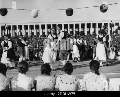 Un gruppo di danza folcloristica in tradizionali balli in costume su un podio rialzato durante il festival folk sul campo di Zeppelin. Sullo sfondo la tribuna Zeppelin. Foto Stock