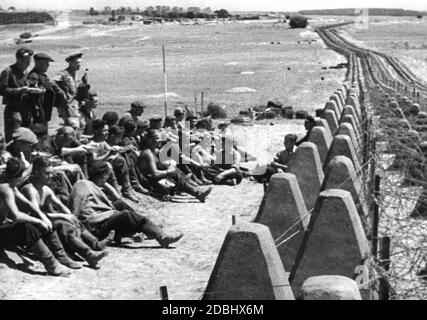 "Un gruppo di lavoratori impegnati nella costruzione durante la pausa pranzo accanto a una linea di barriere anticarro. Scena del documentario 'Der Westwall' (''The West Wall'), un film di propaganda della Deutsche Wochenschau (la rivista settimanale tedesca) presentato all'inizio di agosto 1939. Il film intende presentare il confine occidentale tedesco come un baluardo insormontabile per proteggere la popolazione dagli effetti di una possibile guerra. ' Foto Stock