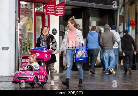 Dundee, Tayside, Scozia, Regno Unito. 17 Nov 2020. Notizie del Regno Unito Covid-19 Lockdown. Le persone che camminano per le strade di Dundee con pochi negozi di abbigliamento essenziali aperti dal livello 3 più rigoroso Covid-19 Lockdown restrizione è stato imposto. Le famiglie sono consapevoli delle linee guida di allontanamento sociale e l'uso di maschere facciali a piedi che portano i nomi di marca borse portarulli mentre si spinge una bambina in un'auto rosa passeggino durante lo shopping di Natale dell'ultimo minuto nel centro della città in un pomeriggio di novembre mite e soleggiato. Credit: Dundee Photographics/Alamy Live News Foto Stock