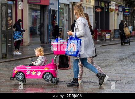 Dundee, Tayside, Scozia, Regno Unito. 17 Nov 2020. Notizie del Regno Unito Covid-19 Lockdown. Le persone che camminano per le strade di Dundee con pochi negozi di abbigliamento essenziali aperti dal livello 3 più rigoroso Covid-19 Lockdown restrizione è stato imposto. Le famiglie sono consapevoli delle linee guida di allontanamento sociale e l'uso di maschere facciali a piedi che portano i nomi di marca borse portarulli mentre si spinge una bambina in un'auto rosa passeggino durante lo shopping di Natale dell'ultimo minuto nel centro della città in un pomeriggio di novembre mite e soleggiato. Credit: Dundee Photographics/Alamy Live News Foto Stock