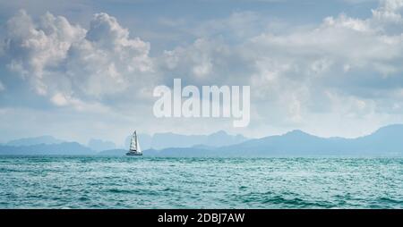 Lone barca a vela nel Mare delle Andamane in Thailandia con la costa di Krabi all'orizzonte Foto Stock