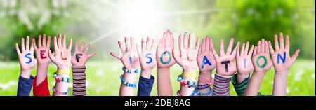 Mani dei bambini che tiene l'auto-isolamento colorato della parola inglese. Prato verde soleggiato come sfondo Foto Stock