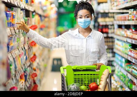 Donna nera che prende il prodotto alimentare facendo acquisti di generi alimentari in supermercato Foto Stock