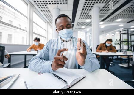 Studente nero che applica l'igienizzatore antibatterico sulle mani Foto Stock