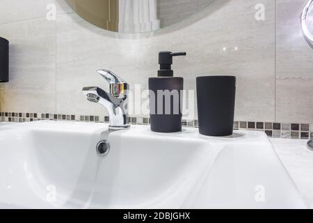 Lavello in ceramica con rubinetto con sapone nero e. distributori di shampoo in bagno costoso Foto Stock